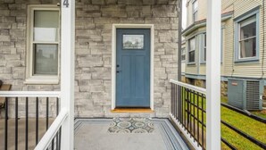 Une maison à deux étages avec une façade en pierre, une porte bleue et un petit porche doté d’une balustrade blanche.