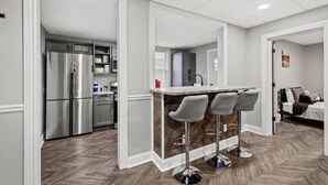 Une cuisine moderne dotée d’appareils électroménagers en acier inoxydable, d’un coin bar avec des tabourets et d’un parquet en bois disposé en chevrons.
