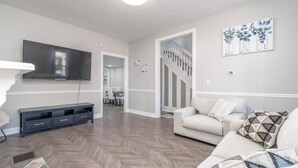 Un salon moderne doté d’un téléviseur à écran plat, d’un canapé, d’une table basse et d’un parquet à motifs en chevrons.