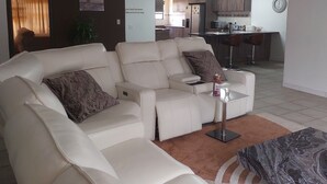 A living room with a sofa, a coffee table, and a ceiling fan. There is a kitchen in the background with cabinets and a microwave. - A staycation in walvis bay
 (walvis bay)