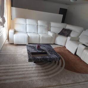 Ein modernes Wohnzimmer mit einem weißen Ledersofa, einem Marmor-Couchtisch und einem gemusterten Teppich.