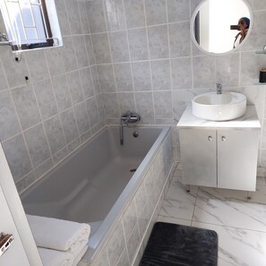 Ein modernes Badezimmer mit Badewanne, rundem Spiegel und weißem Waschbecken.