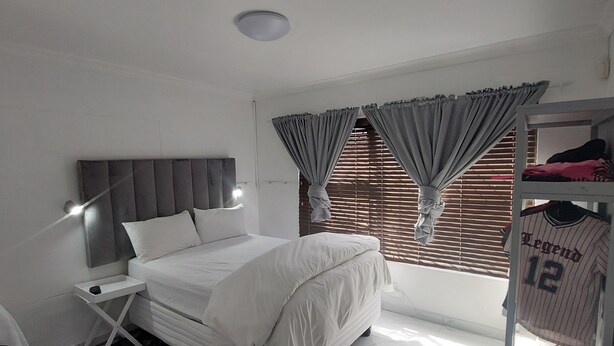 A bedroom with a bed, a bedside table, a wardrobe, and a window with curtains. - A staycation in walvis bay
 (walvis bay)