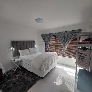 A bedroom with a bed, a bedside table, a wardrobe, and a window with curtains. - A staycation in walvis bay
(walvis bay)