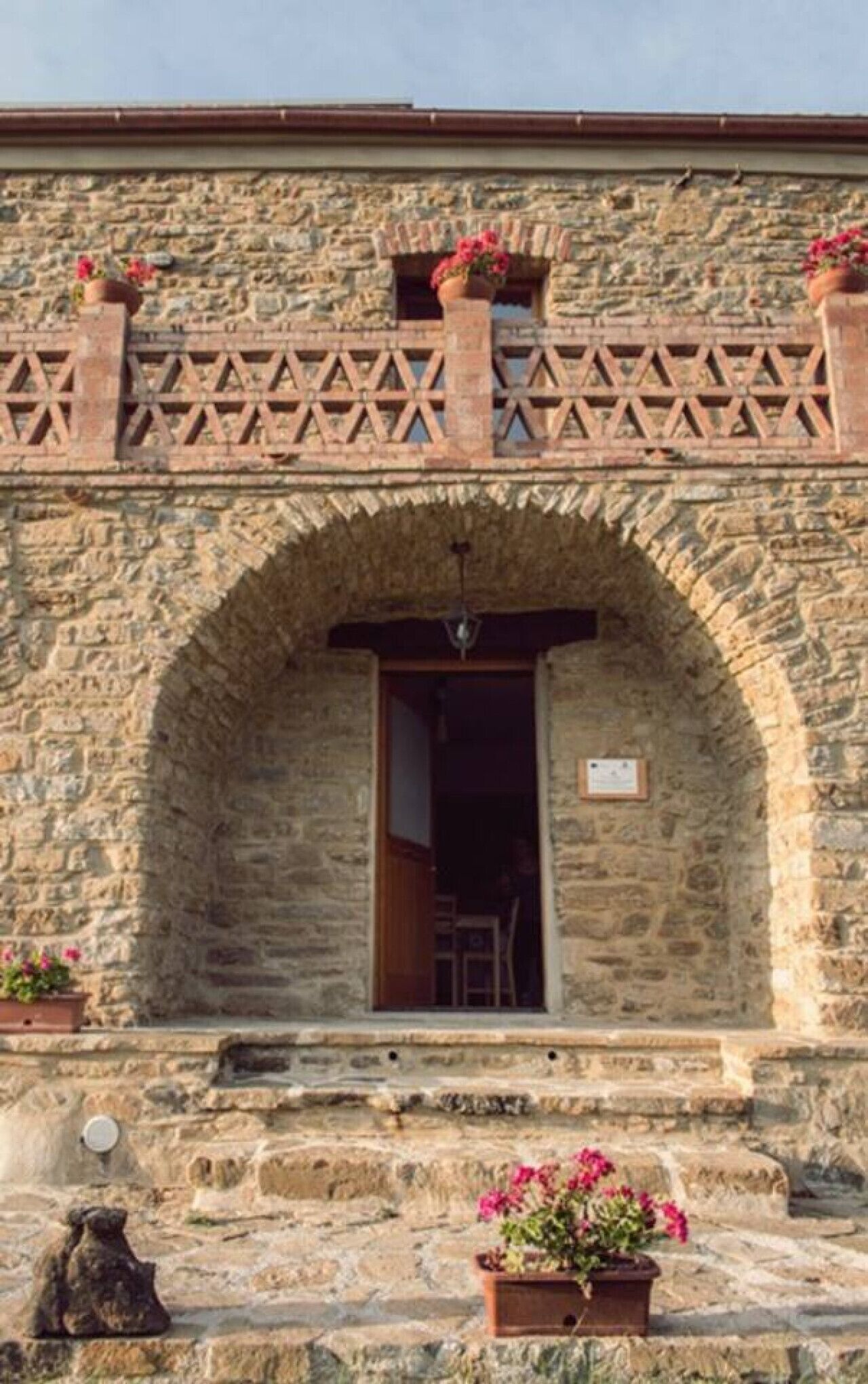 A stone building with an arched doorway, a small balcony with lattice railings, and potted plants.
