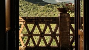 Porta aberta que dá para uma varanda com vista para uma paisagem montanhosa e um céu nublado.