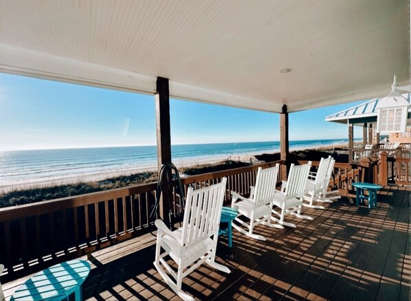 A covered outdoor area with white rocking chairs and a table, overlooking the beach. - Turtle's Pace - a 5 bed, 3.5 bath Oceanfront pet friendly (North Topsail Beach)