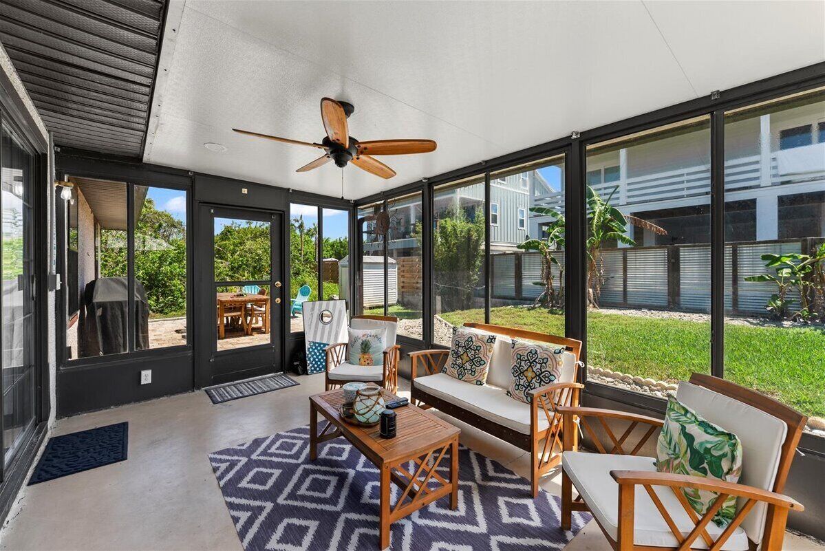 Screened-in patio with cozy seating, ceiling fan, and peaceful backyard views.