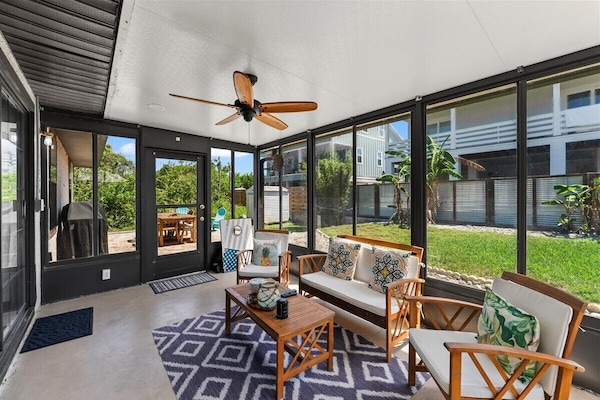 Screened-in patio with cozy seating, ceiling fan, and peaceful backyard views.