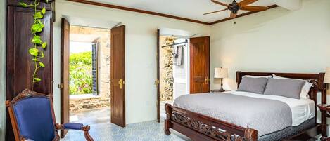 Un dormitorio con una cama grande, una silla, un ventilador de techo y vistas al exterior.