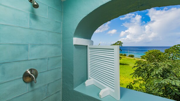 A bathroom with teal tiles, a shower, and a view of the ocean.