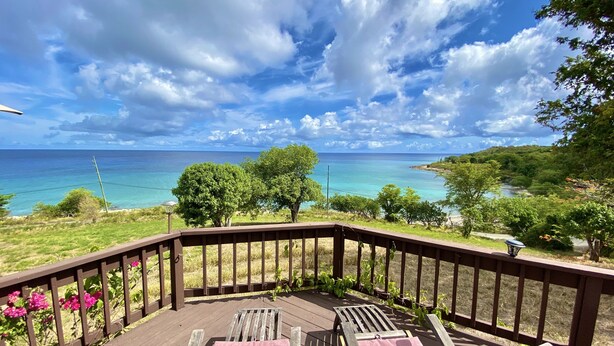 Une terrasse en bois avec deux chaises longues et une table, offrant une vue sur une mer turquoise et un paysage luxuriant.