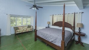 Un lit à baldaquin avec une tête de lit en bois, un ventilateur de plafond et une fenêtre avec des volets.