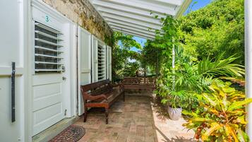 Une terrasse couverte avec un banc, une porte à volets et des plantes en pot.