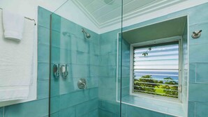 Une salle de bain avec des carreaux bleus, une douche en verre, une fenêtre donnant sur la verdure et une serviette accrochée au mur.