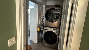 Une buanderie équipée d’un lave-linge et d’un sèche-linge, d’un panier en osier et d’une petite table contenant des produits de nettoyage.