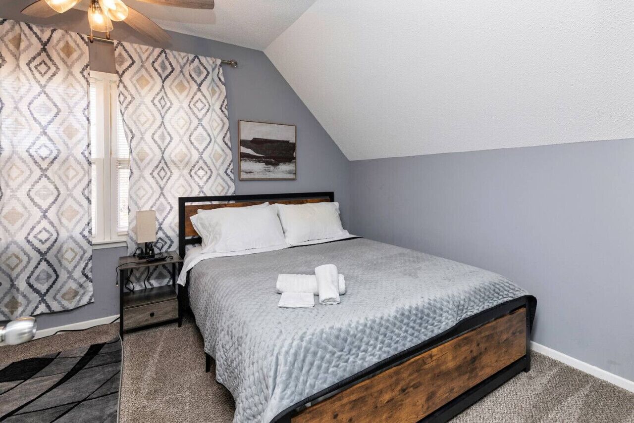 A bedroom with a bed, a nightstand, a lamp, a patterned curtain, and a painting on the wall.