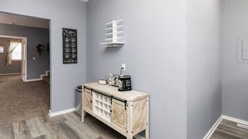 Un couloir avec un mur gris, une console en bois sur laquelle se trouve une machine à café, et un panneau affichant des pictogrammes représentant les différentes sortes de café.