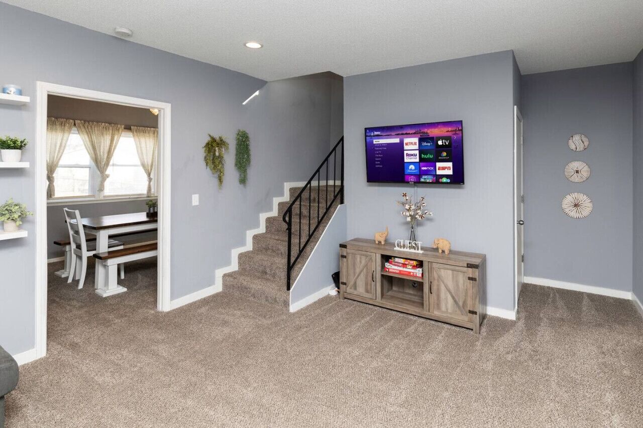 Un salon avec un escalier, un téléviseur fixé au mur et une console en bois.