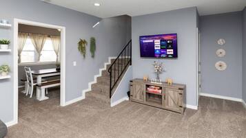 Un salon avec un escalier, un téléviseur fixé au mur et une console en bois.