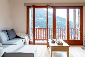 Ein Zimmer mit einer Couch, einem Tisch und einem Balkon mit Bergblick.