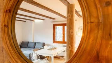 Una habitación con techo de madera, una mesa blanca, un sofá gris y una ventana que da al exterior.