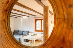 Una habitación con techo de madera, una mesa blanca, un sofá gris y una ventana que da al exterior.
