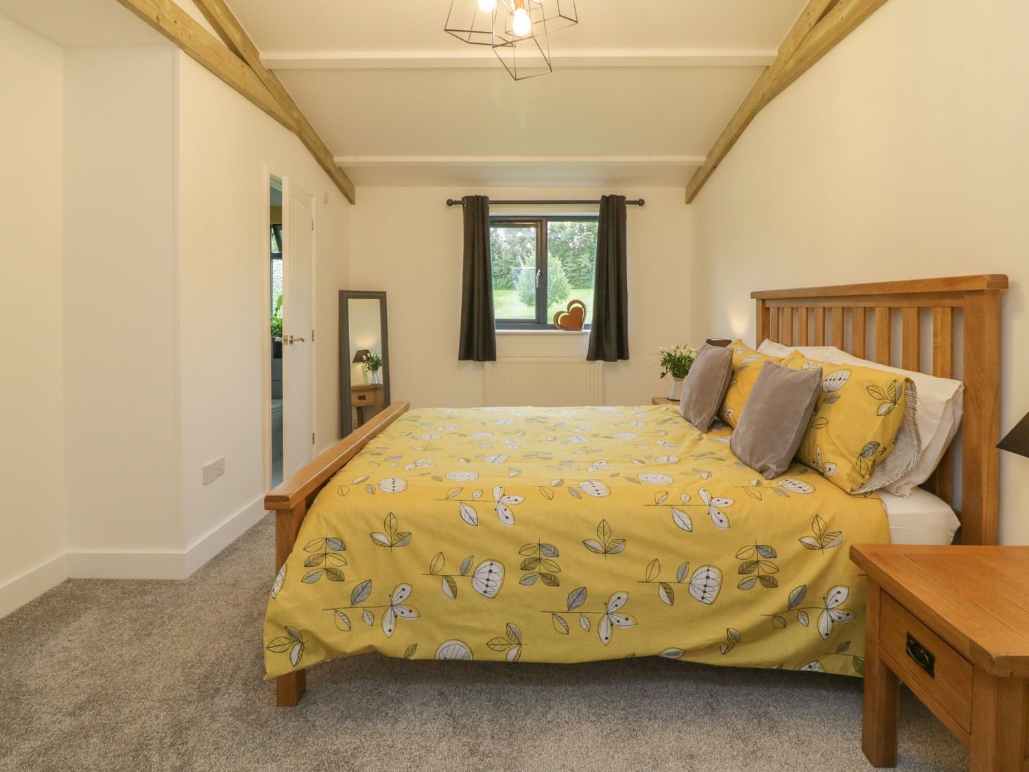 Un dormitorio con cama, mesita de noche, ventana con cortinas y vistas a zonas verdes.