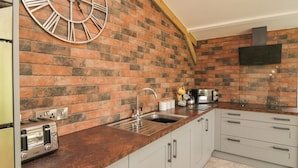 A kitchen with a brick backsplash, a stainless steel sink, a toaster, and a clock.