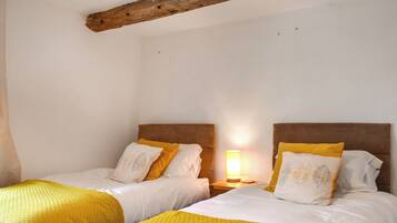 A room with two beds, each with a headboard and a bedside table with a lamp.