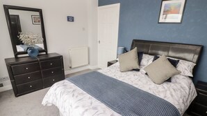 A bedroom with a bed, dresser, mirror, radiator, and a framed picture on the wall. - 54 Croft Court (Tenby)