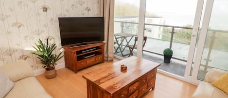 A living room with a wooden coffee table, a sofa, a TV on a wooden stand, and a balcony with a view.