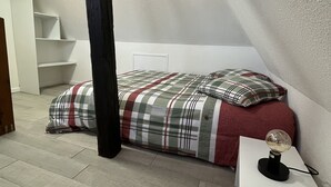 A bedroom with a bed, a nightstand, a wooden beam, and a white wall. - Appartement F2 Duplex Turckheim, Alsace Situé sur la Route des Vins (Turckheim)