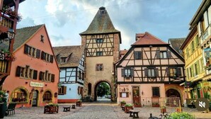 A cobblestone street with traditional half-timbered buildings, an archway, and outdoor seating areas. - Appartement F2 Duplex Turckheim, Alsace Situé sur la Route des Vins (Turckheim)