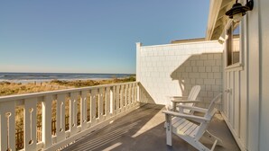 Ein Balkon mit weißen Geländern, zwei Adirondack-Stühlen und Blick auf den Strand.