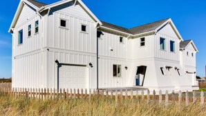 Ein weißes, zweistöckiges Haus mit Garage, Veranda und einem weißen Zaun.