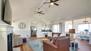A spacious living room with a brown leather sofa, a wooden coffee table, and a blue patterned rug. There are ceiling fans, a fireplace, and a kitchen in the background. - Beachfront Bandon Vacation Rental w/ Ocean View! (Bandon)