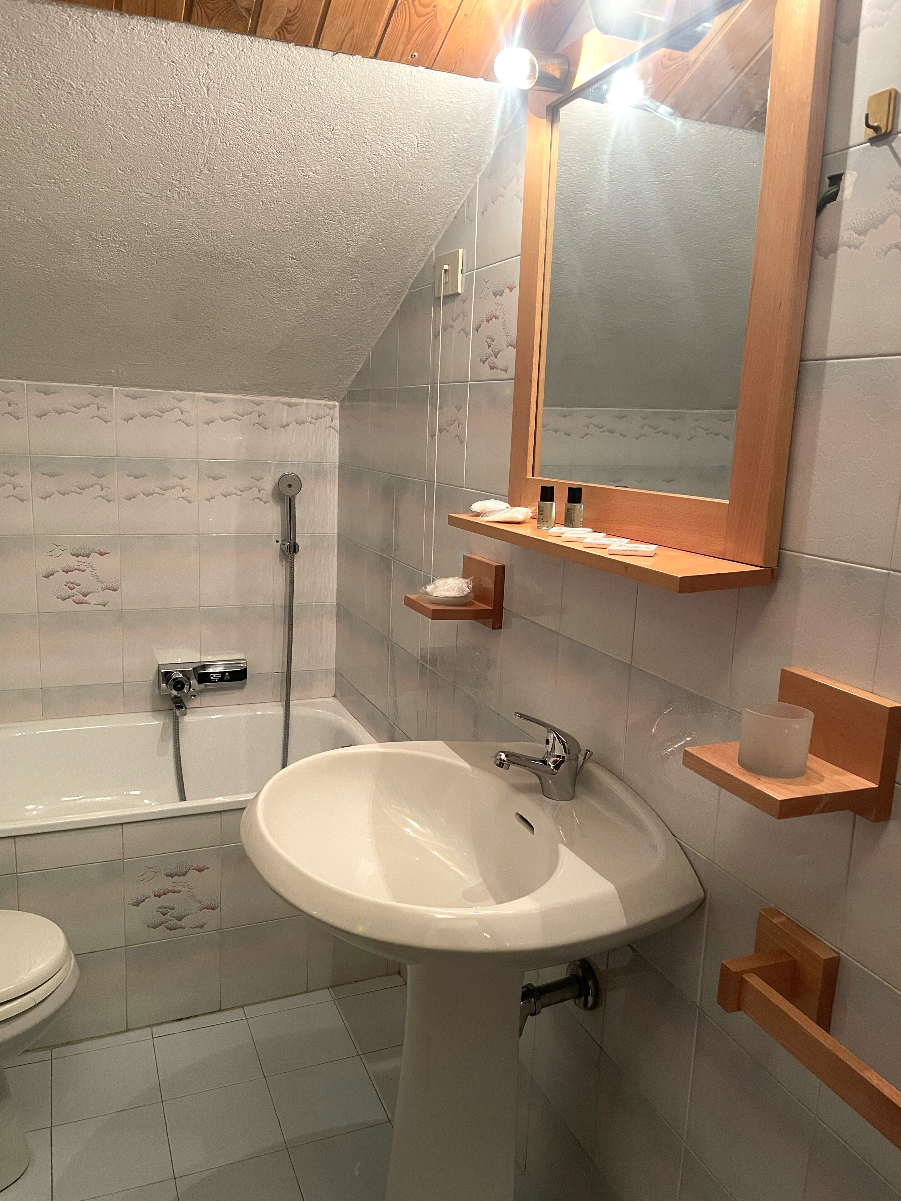 A bathroom with a bathtub, a sink, and a toilet. There is a mirror above the sink and a shelf with toiletries.