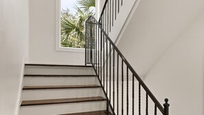 A staircase with dark wooden steps and black metal railings, leading to a room with a large window and a view of palm trees.