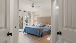A bedroom with a bed, a ceiling fan, and a view of the outdoors through a glass door.