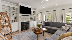 A living room with a fireplace, a television mounted above it, a sofa, and a ceiling fan.