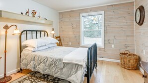 Une chambre à coucher avec un lit, une lampe de chevet, un lambris en bois, une fenêtre et une horloge.