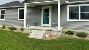 A residential house with a covered porch, two chairs, and a small dog.