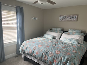 A bedroom with a bed, curtains, a ceiling fan, and a wall sign.