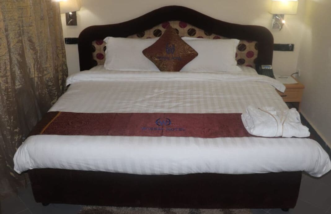 A bed with a headboard, a blanket, and a pillow with a logo.