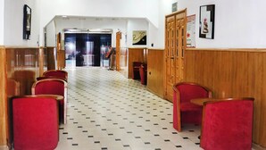 Un vestíbulo de hotel con piso a cuadros, sillas rojas, paneles de madera y una puerta que da a otra zona.