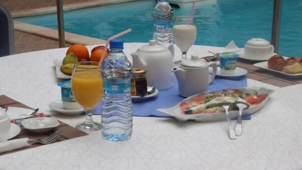 Una mesa de desayuno con una variedad de alimentos y bebidas, incluyendo un plato de ensalada, una jarra de jugo de naranja y una botella de agua.