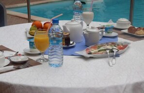 Una mesa de desayuno con una variedad de alimentos y bebidas, incluyendo un plato de ensalada, una jarra de jugo de naranja y una botella de agua.
