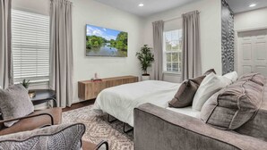 Une chambre à coucher comprenant un lit, un canapé, une chaise, une table de chevet, une plante et un tableau représentant un paysage.