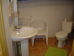 Un baño con un lavamanos blanco, un inodoro blanco y una silla de plástico blanca.